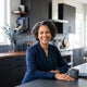 A smiling, diverse woman looking at the camera in a modern, professionally-lit kitchen with slate and charcoal tones.